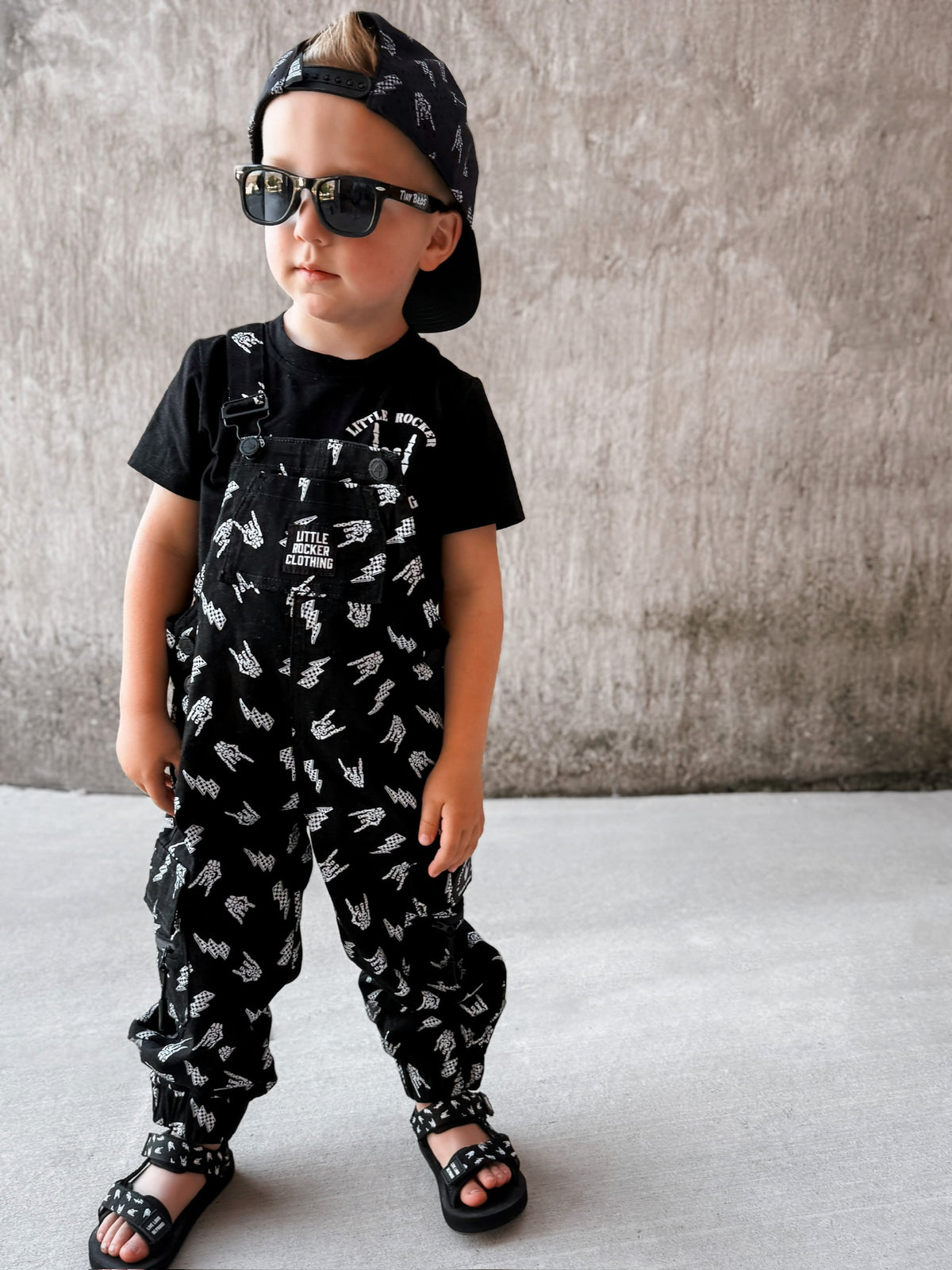 boy wearing kids black bolted bones overalls with lightning bolt and rock hand print matching outfits toddler streetwear little rocker clothing
