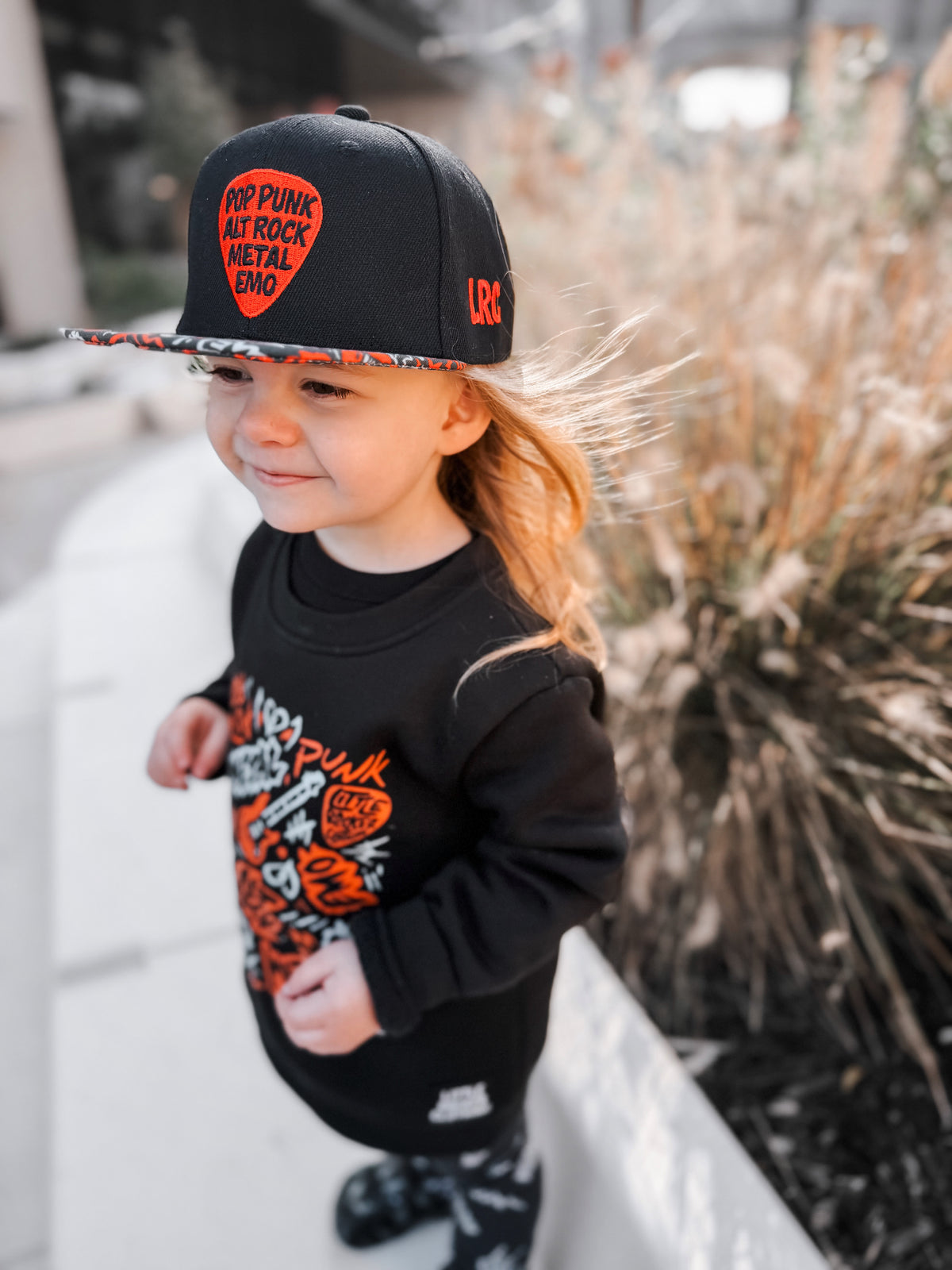 Kid wearing black and red Scene Sampler snapback hat featuring bold music inspired design, adjustable snapback cap for kids and adults, edgy rock style apparel accessory