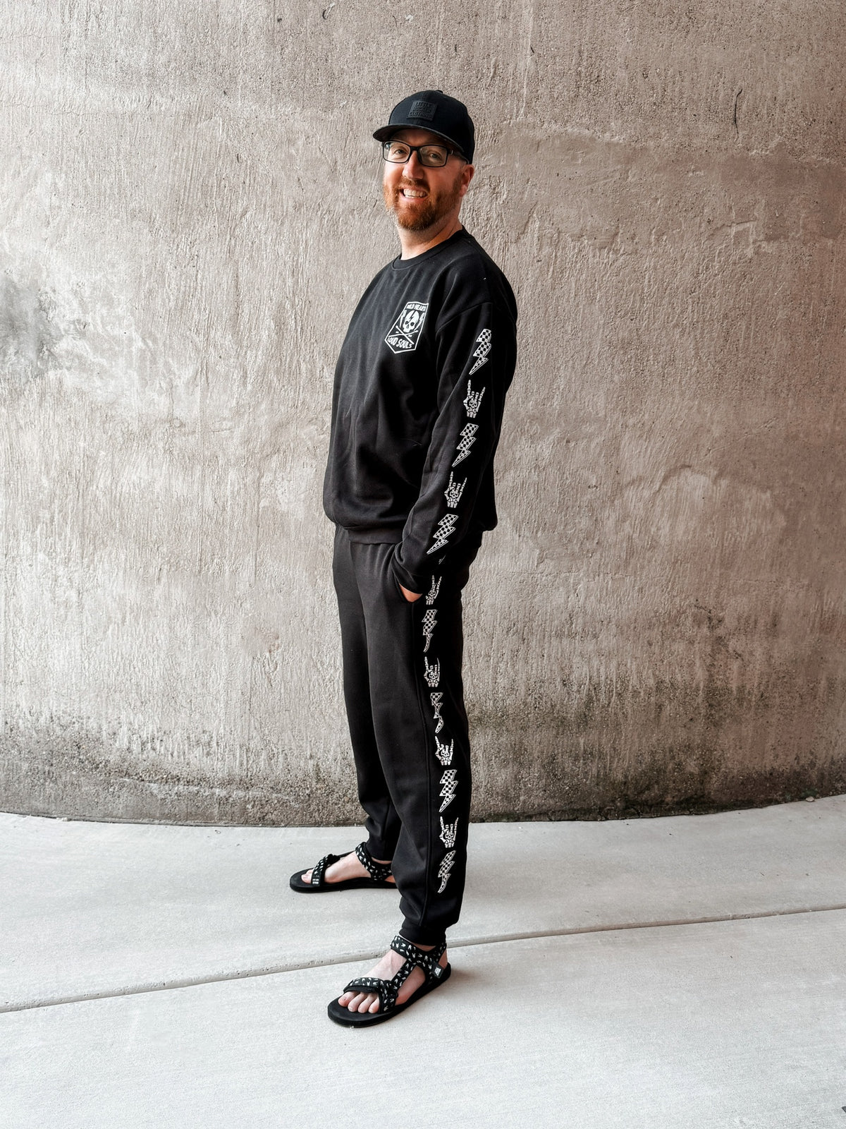 dad wearing matching black aftershock crew neck sweatshirts and joggers set lightning bolt and rock hand print little rocker clothing adult and kids outfits