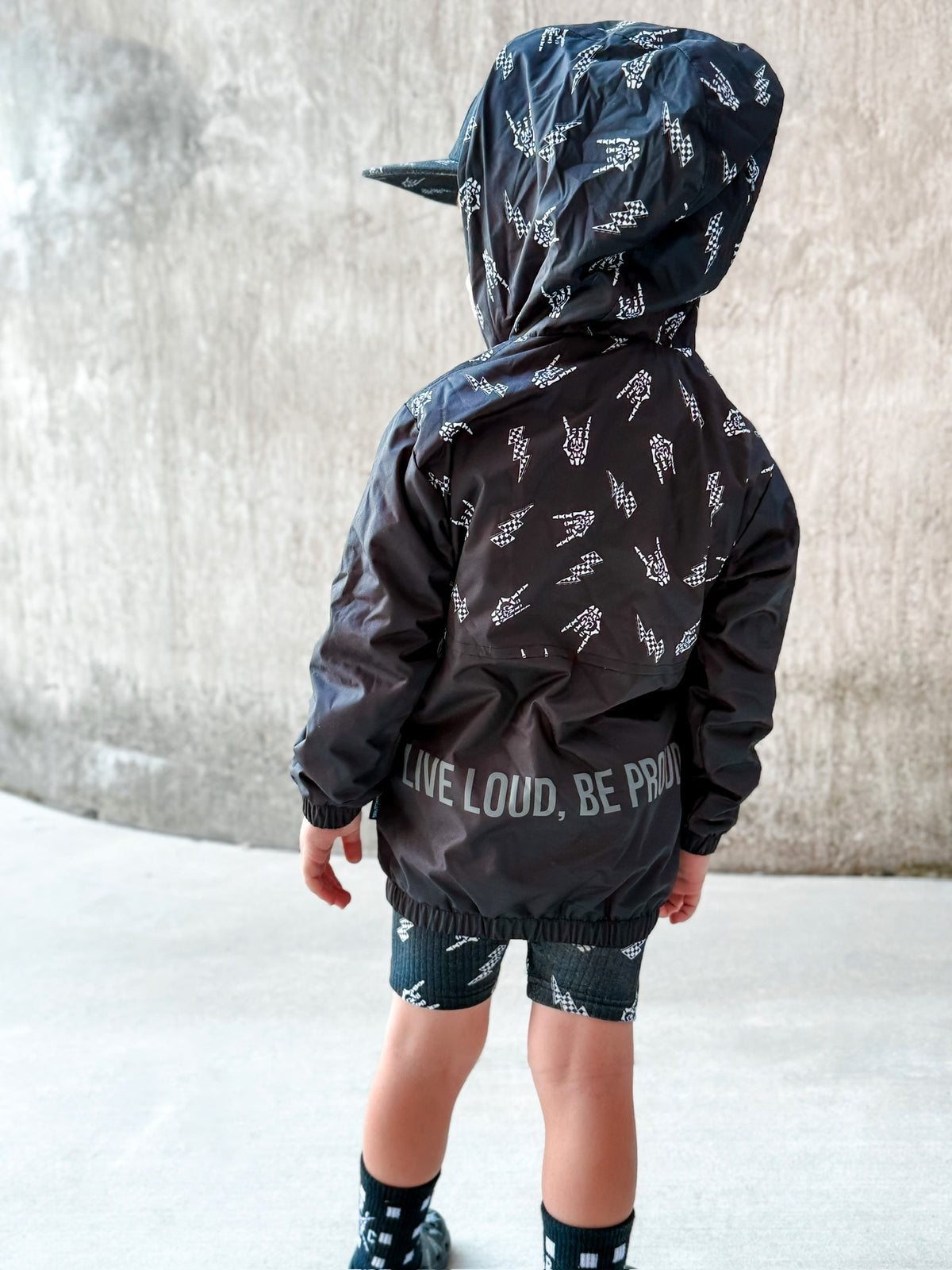 Kids bolted bones black windbreaker jacket with all over graphic print, live loud be proud on back side of the lightweight rocker style outerwear for kids with zip front and hood