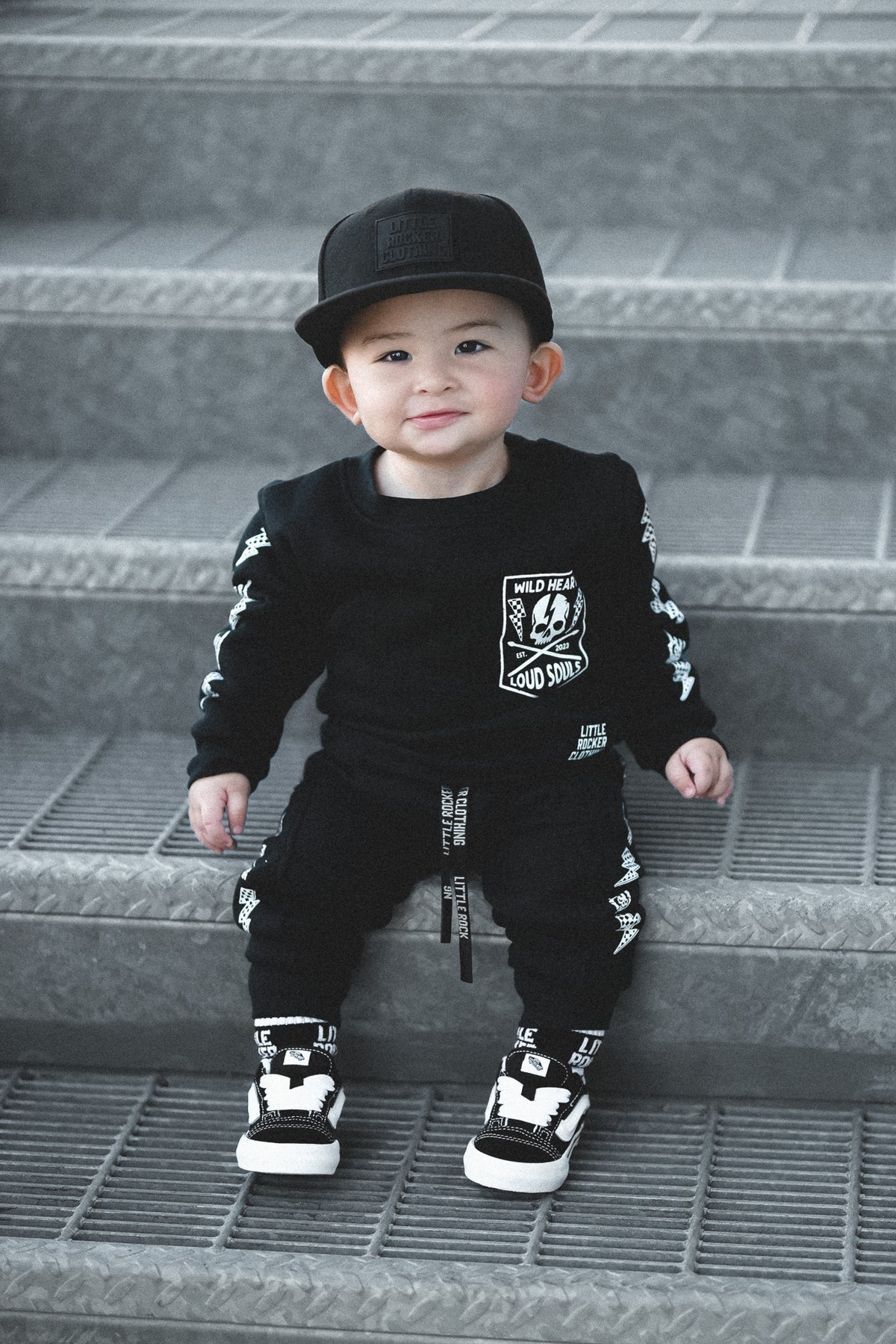 infant wearing matching black aftershock crew neck sweatshirts and joggers set lightning bolt and rock hand print little rocker clothing adult and kids outfits