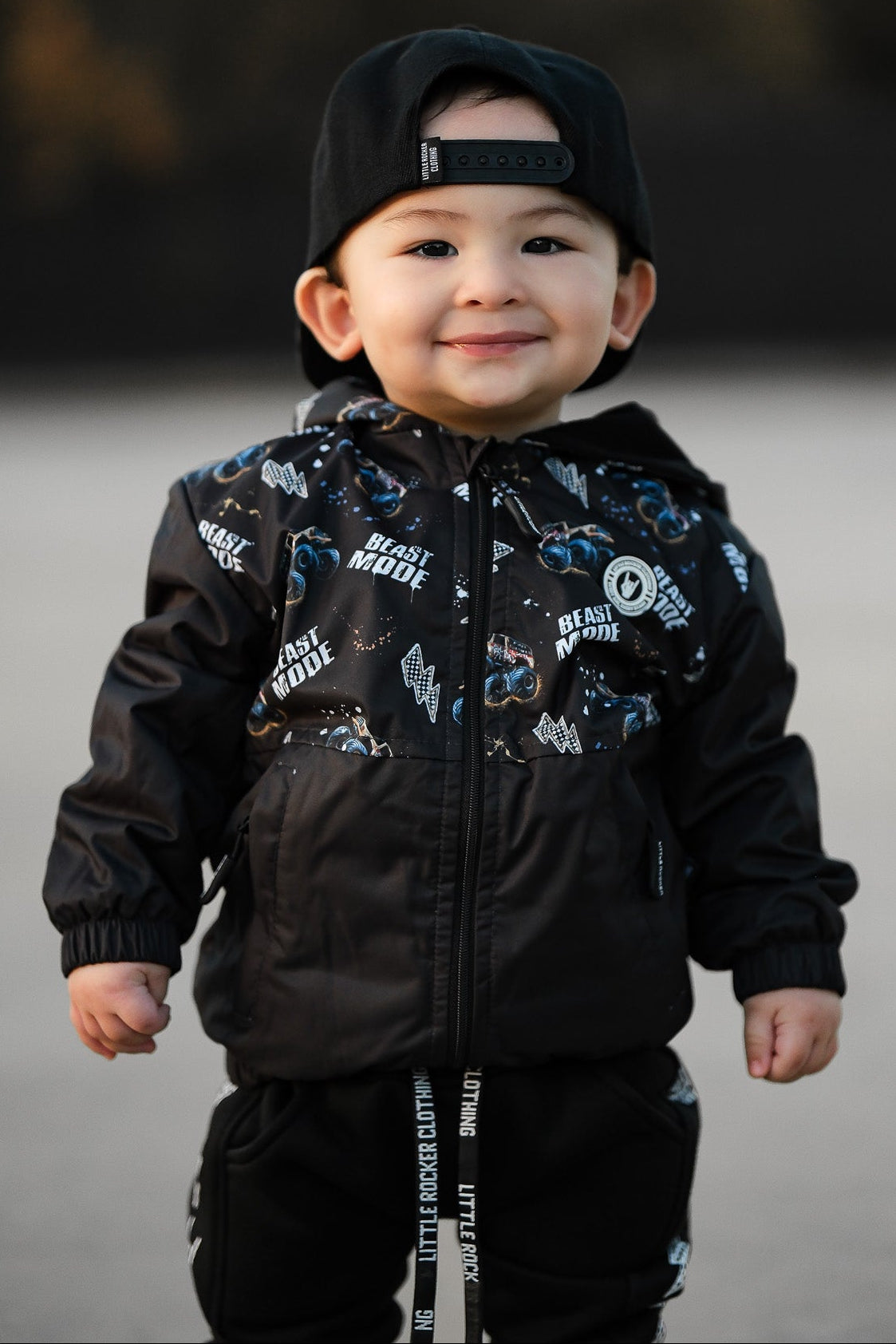 Young child wearing Kids Beast Mode black windbreaker jacket with all over graphic print, lightweight rocker style outerwear for kids with zip front and hood