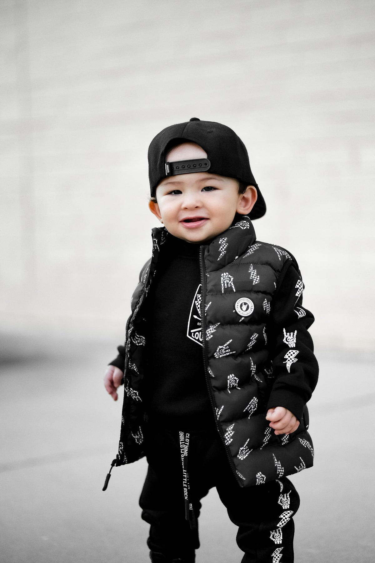 Young child wearing Kids black puffer vest with Bolted Bones design featuring skeleton hand rock on graphic and lightning bolts, rocker style outerwear for kids