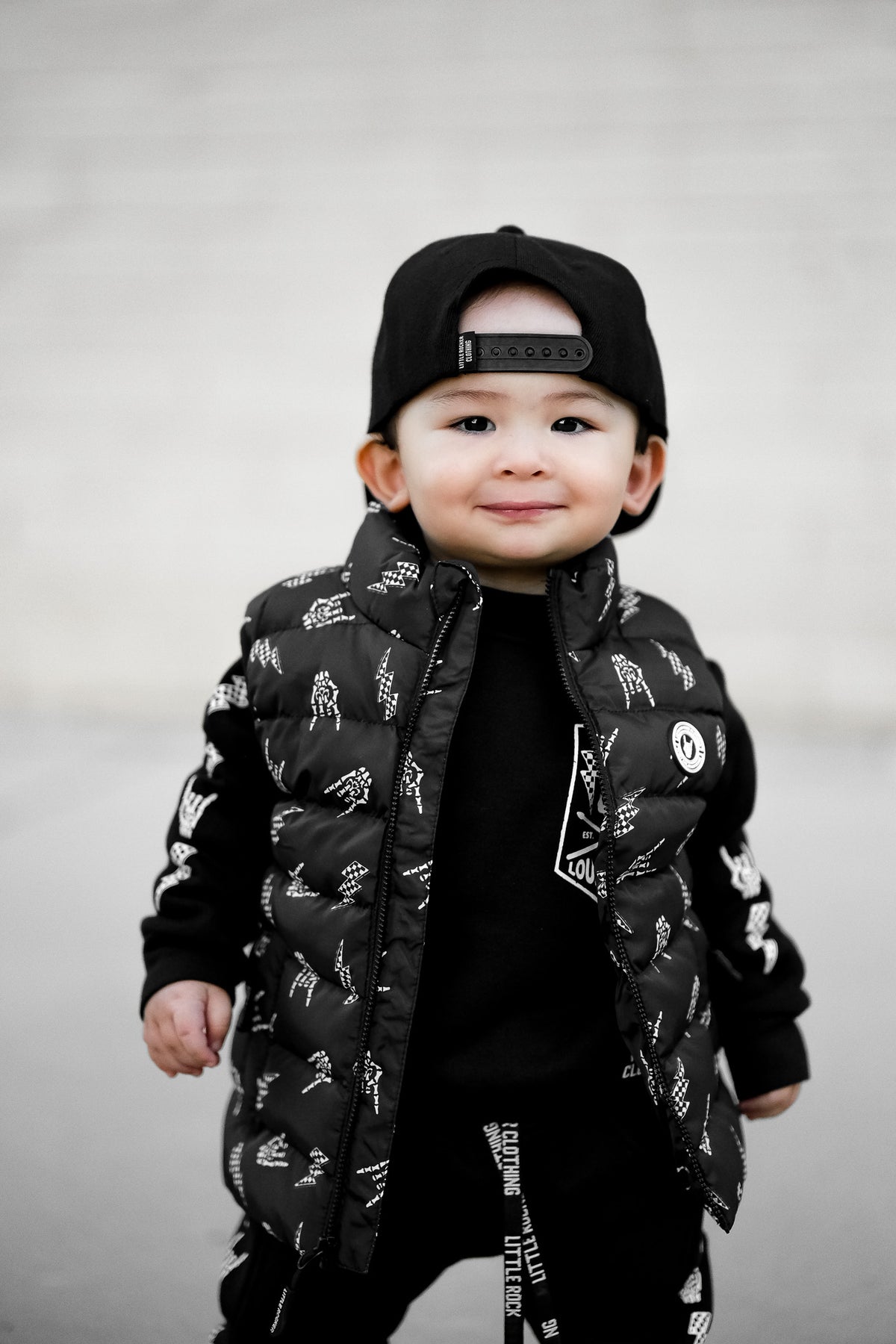 Young boy wearing the Kids black puffer vest with Bolted Bones design featuring skeleton hand rock on graphic and lightning bolts, rocker style outerwear for kids