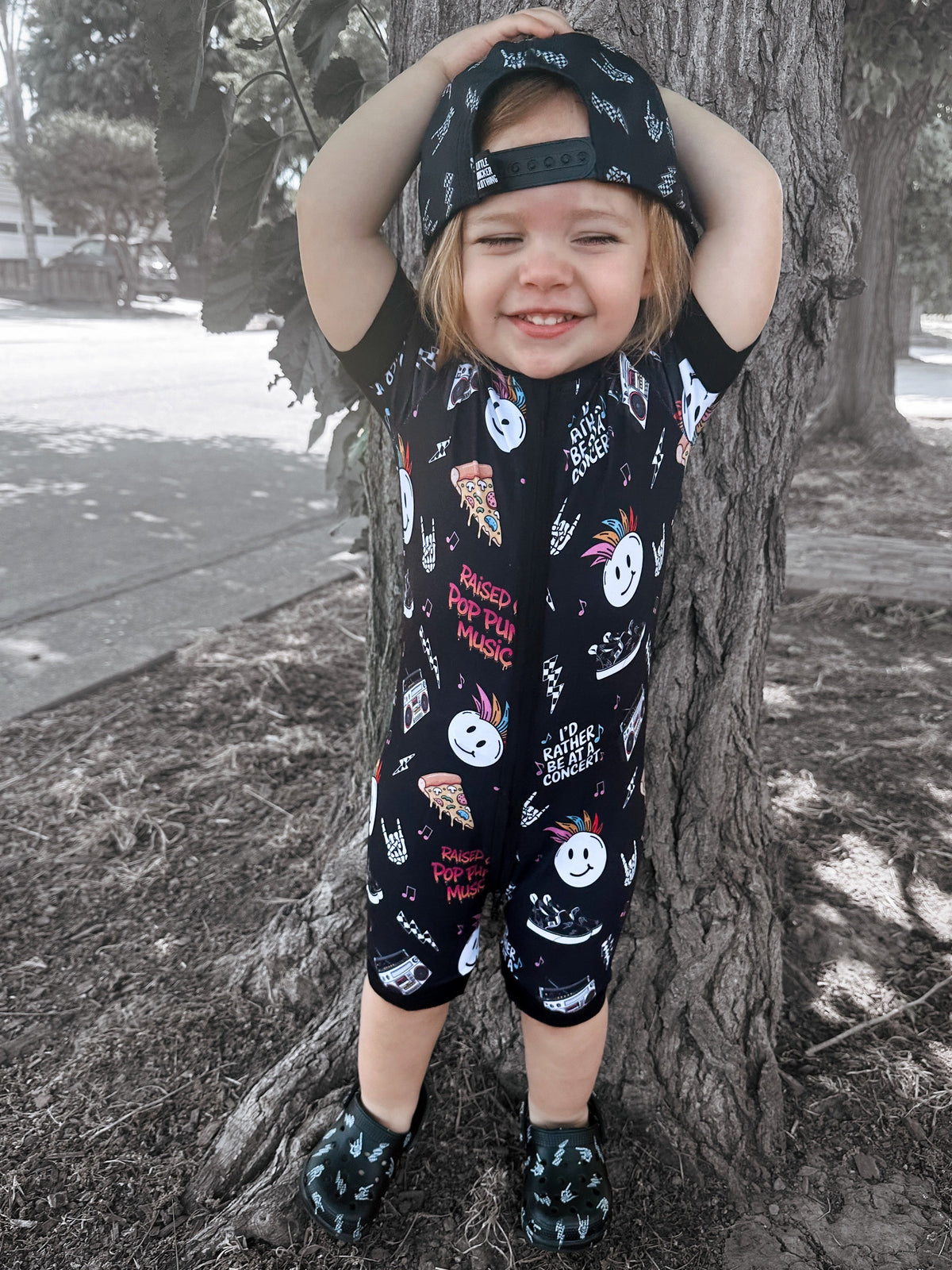 toddler wearing pop punk collage pattern short sleeve zip up bamboo pajamas for kids paired with black snapback