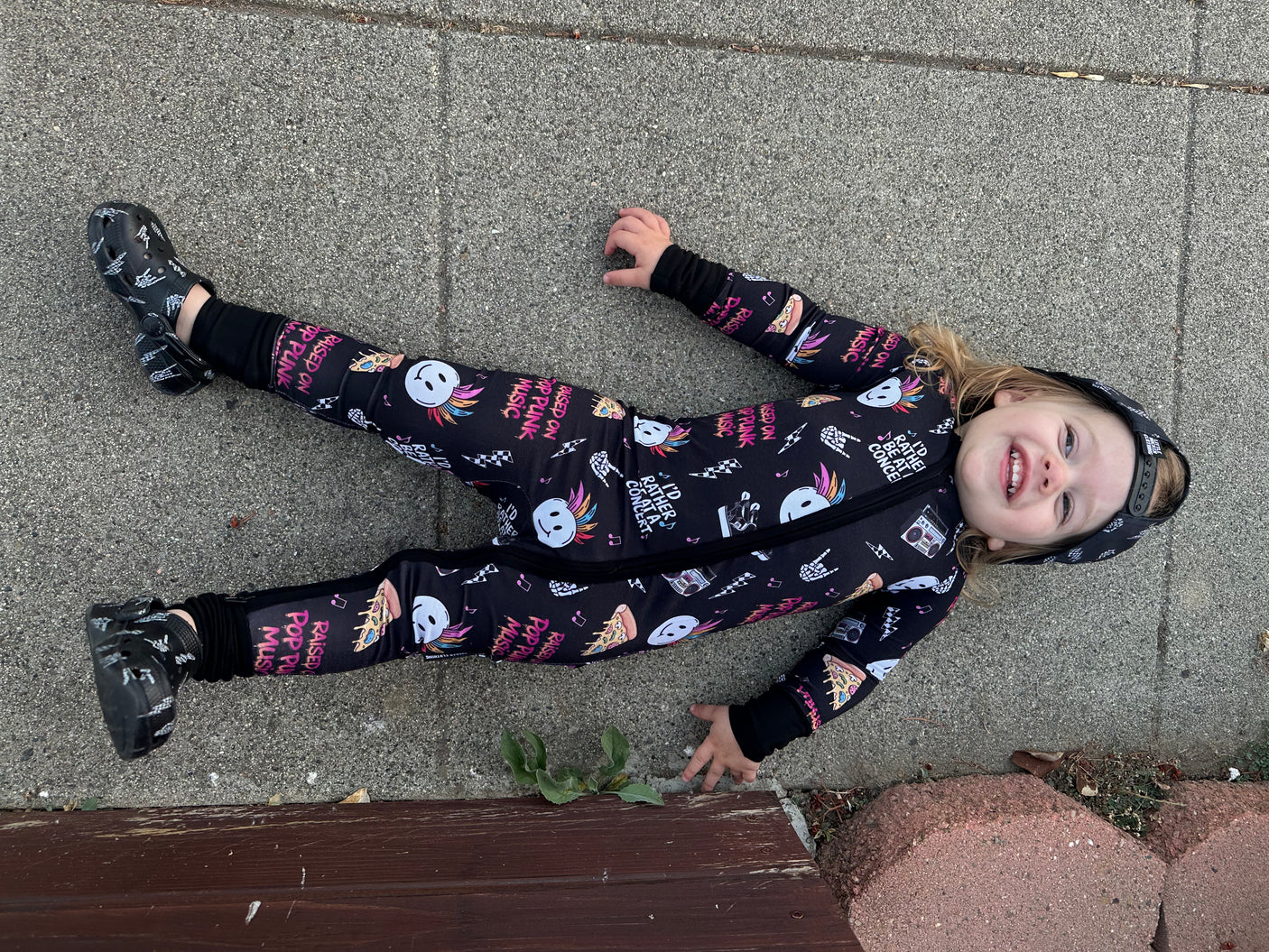 toddler laying on ground wearing pop punk collage pattern long sleeve zip up bamboo pajamas for kids