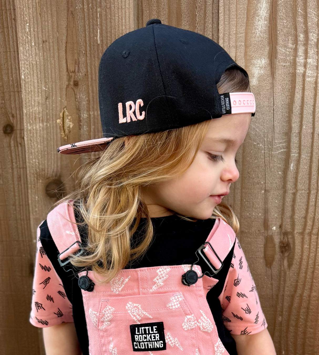 Kid wearing pink and black rock on snapback hat, adjustable snapback cap for kids and adults, edgy music inspired apparel accessory