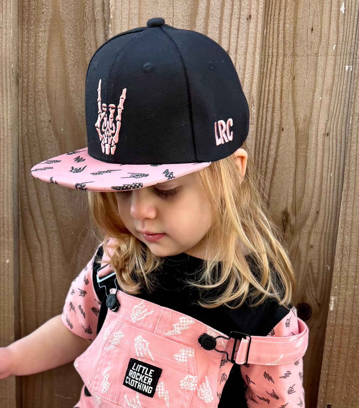 Kid wearing Little Rocker Clothing pink and black rock on snapback hat, adjustable snapback cap for kids and adults, edgy music inspired apparel accessory