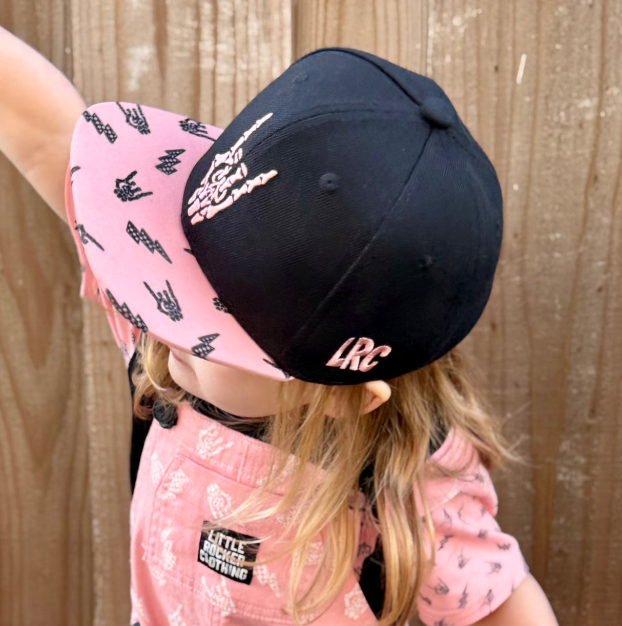 Kid wearing pink and black rock on snapback hat, adjustable snapback cap for kids and adults, edgy music inspired apparel accessory