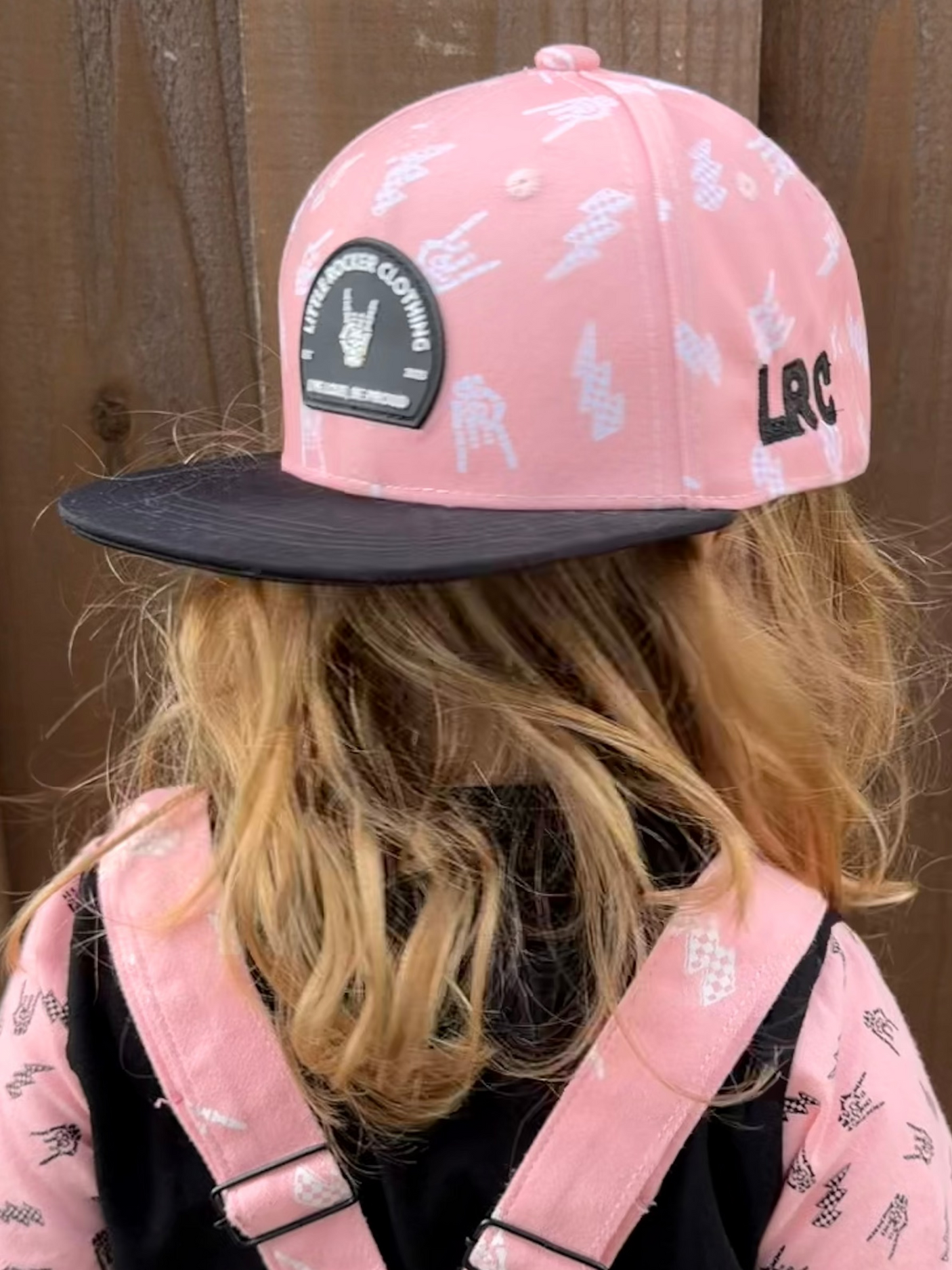 Kid wearing Little Rocker Clothing pink and black rock on and lightening bolt snapback hat, adjustable snapback cap for kids and adults, edgy music inspired apparel accessory
