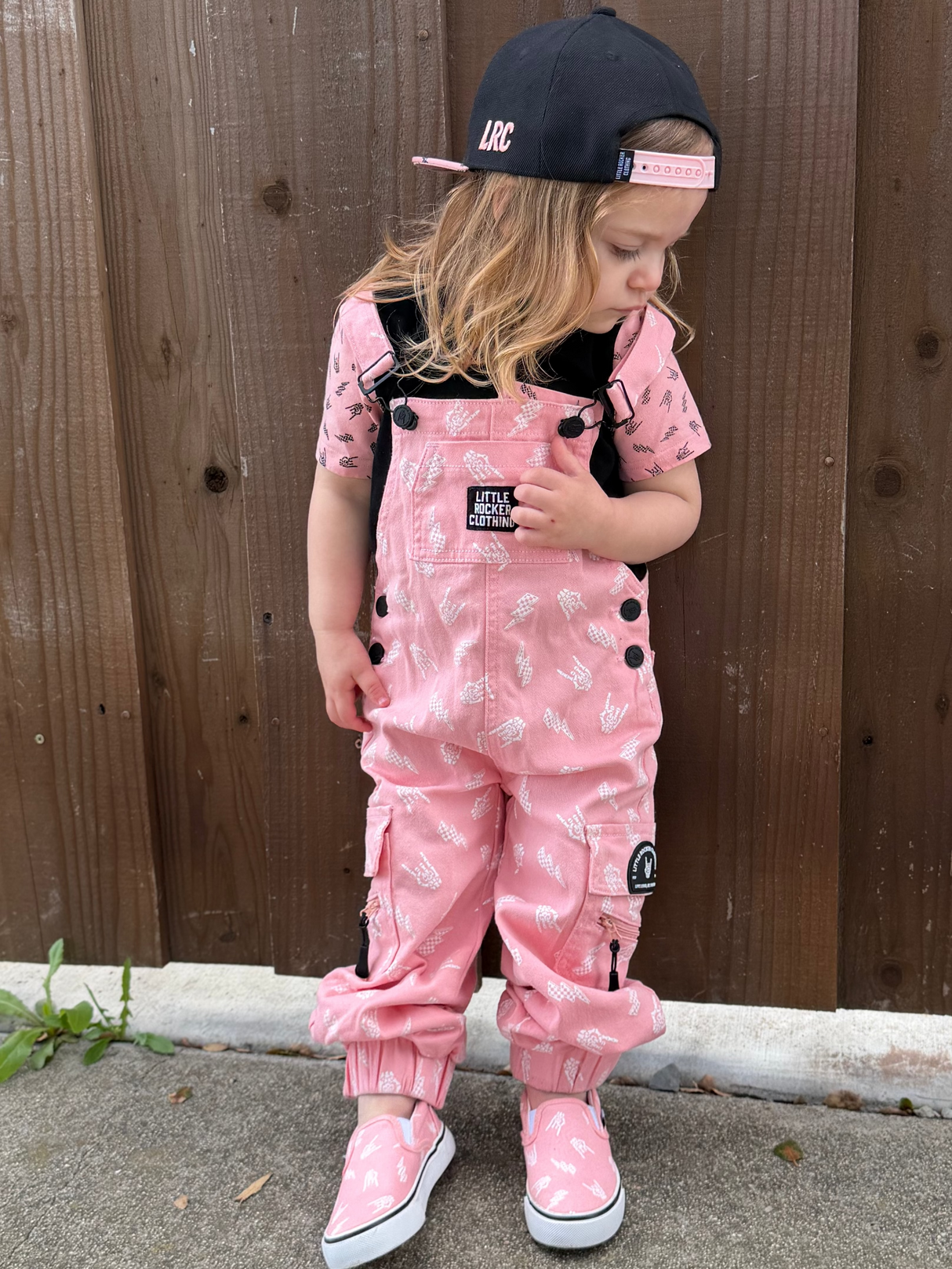 young girl wearing pink overalls with rock on horns and lightening bolts from little rocker clothing