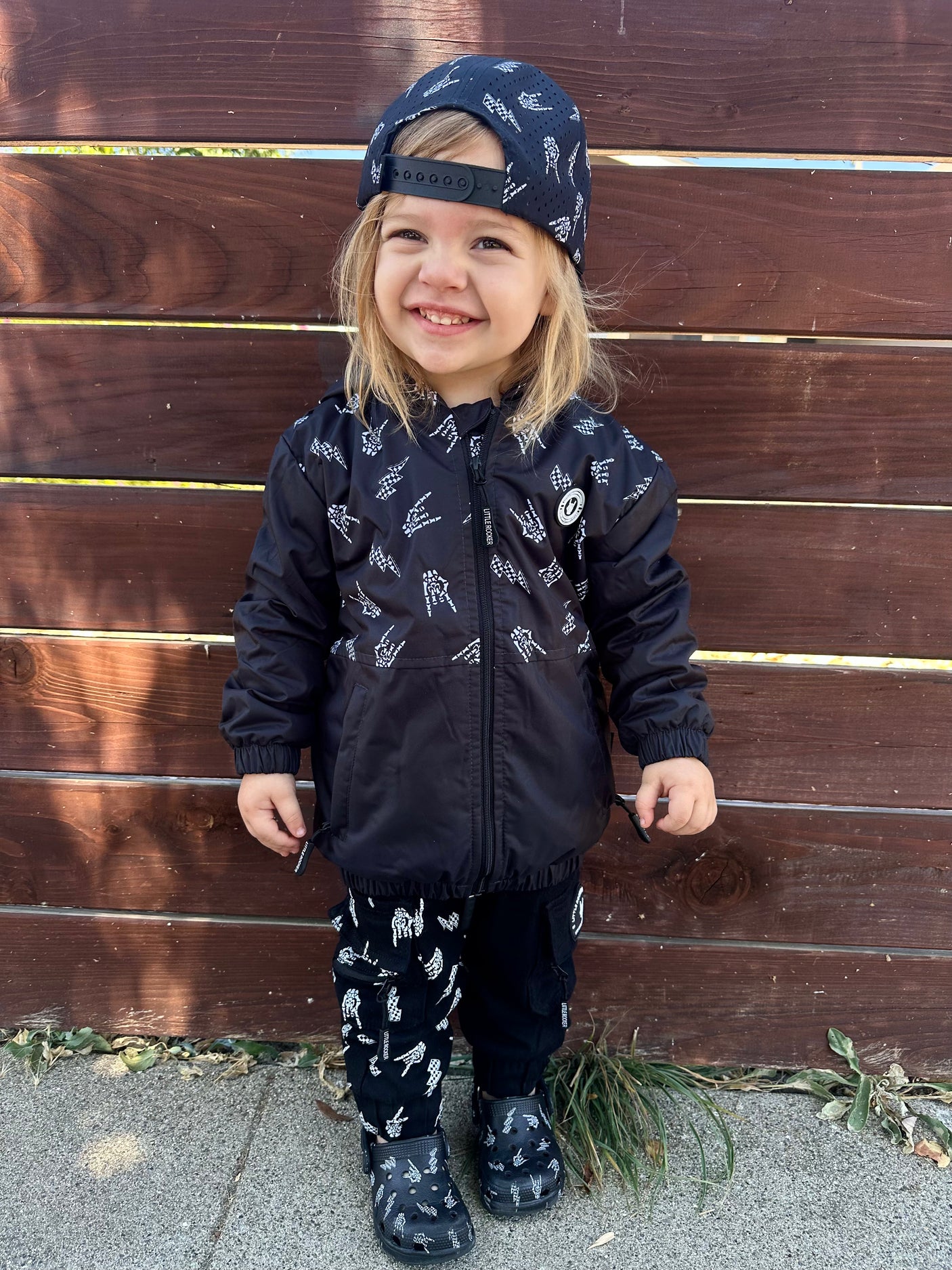 Toddler girl wearing Kids bolted bones black windbreaker jacket with all over graphic print, lightweight rocker style outerwear for kids with zip front and hood