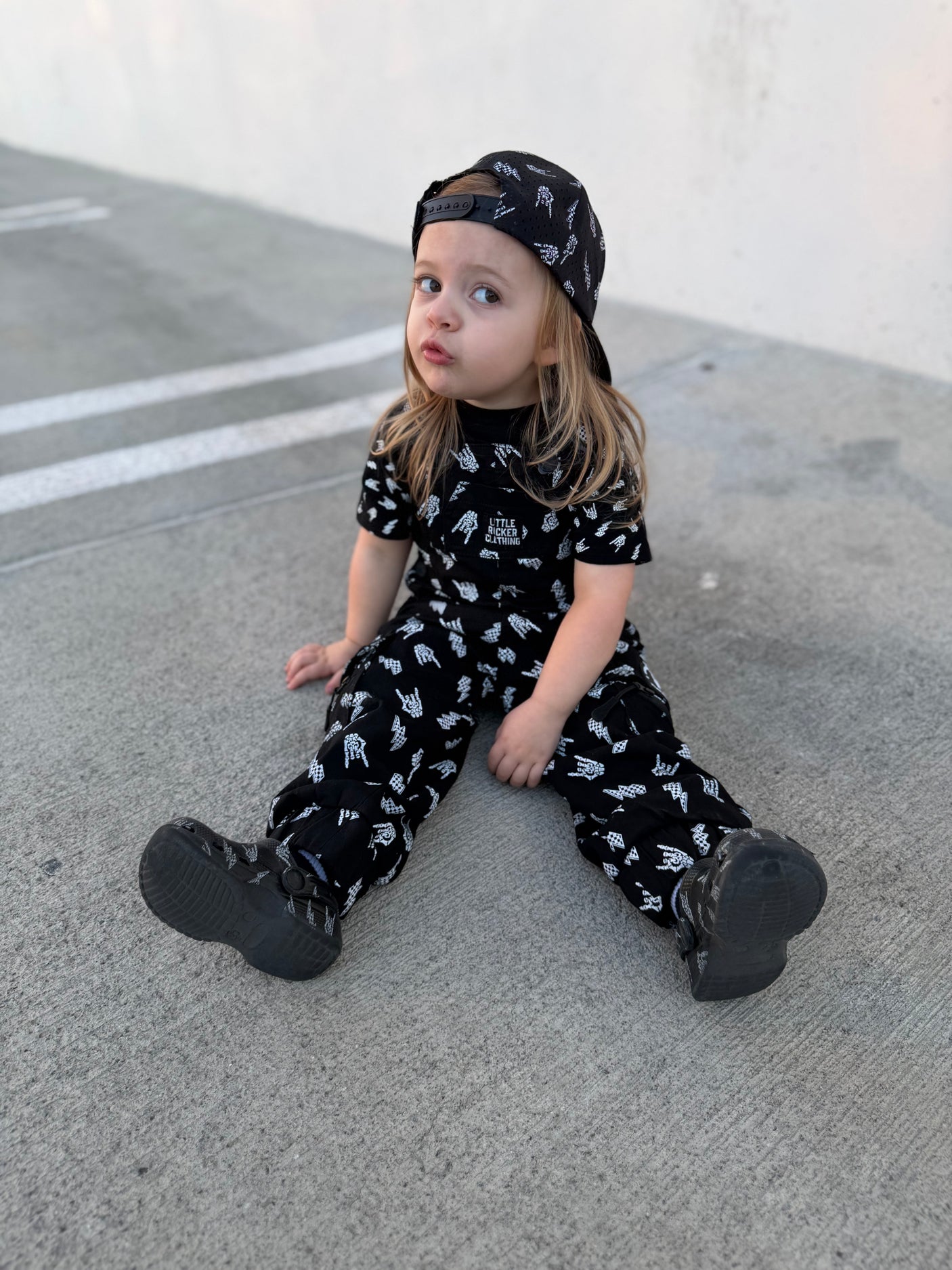 girl wearing kids black bolted bones overalls with lightning bolt and rock hand print matching outfits toddler streetwear little rocker clothing