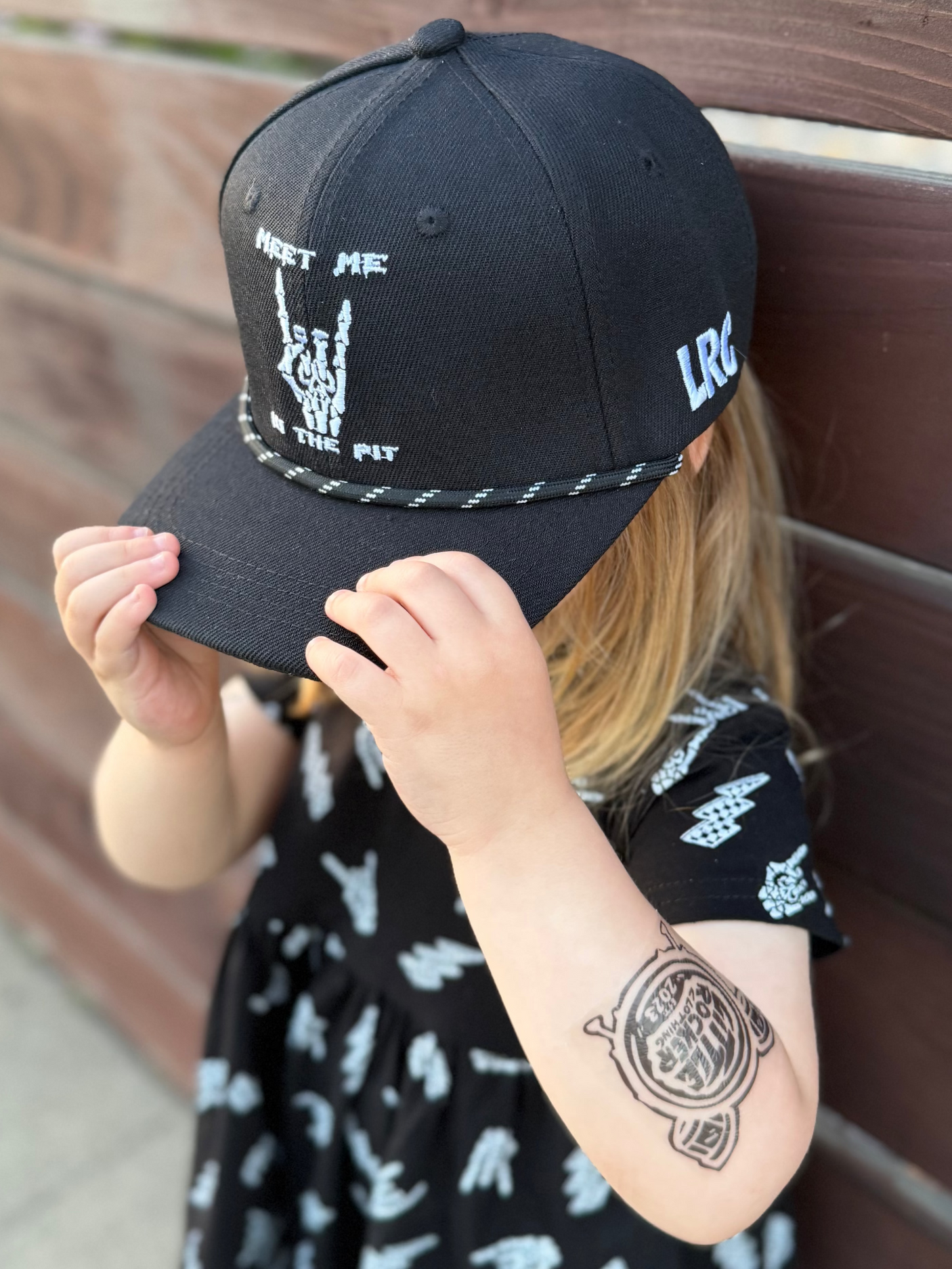 Kid wearing Little Rocker Clothing meet me in the pit black snapback hat, adjustable snapback cap for kids and adults, edgy rock music inspired apparel accessory