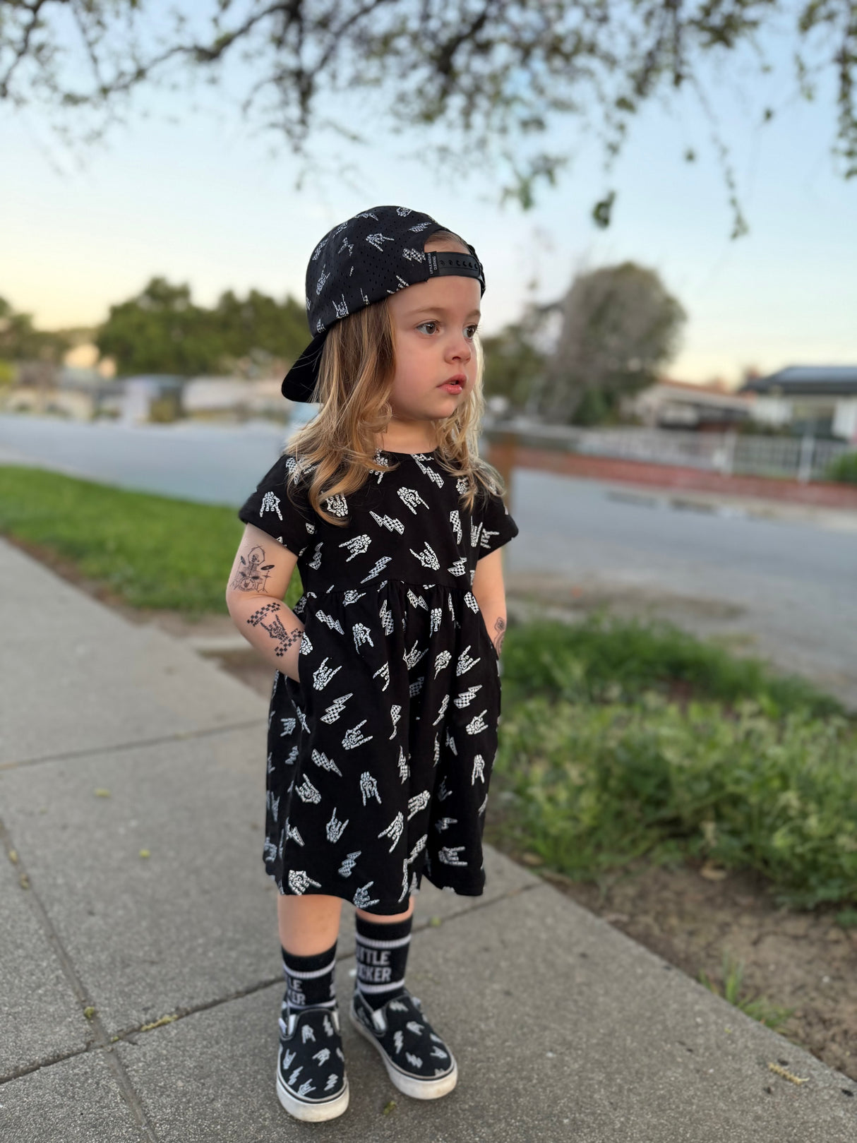 young girl wearing bolted bones pattern black dress with hands in pockets