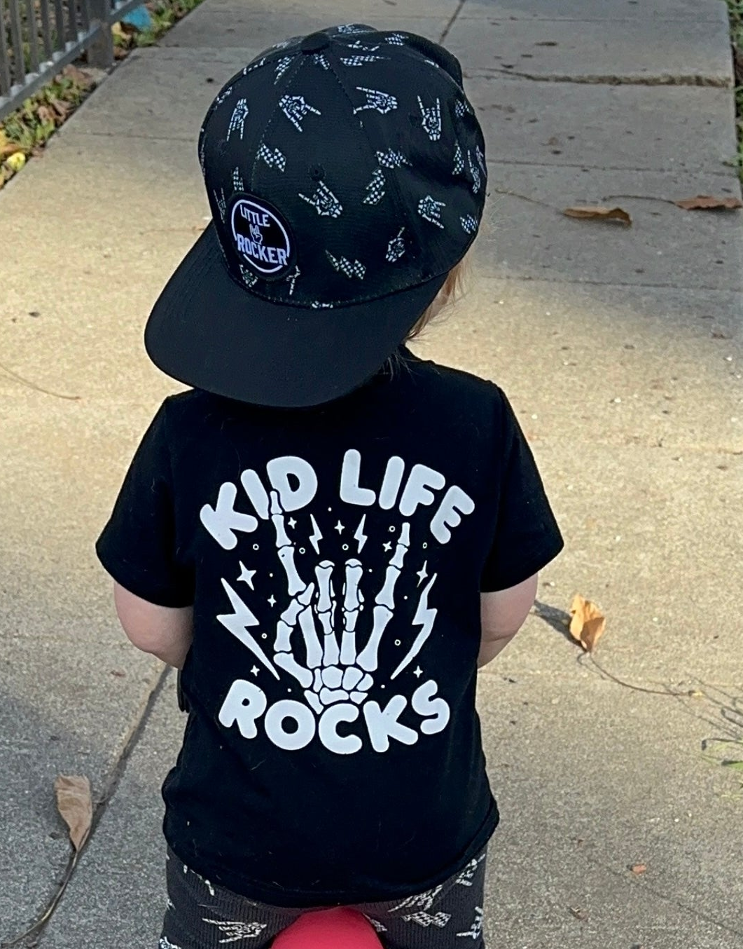 black kids graphic t-shirt with kid life rocks, little rocker clothing rock style outfit for toddlers and kids outdoors rear view
