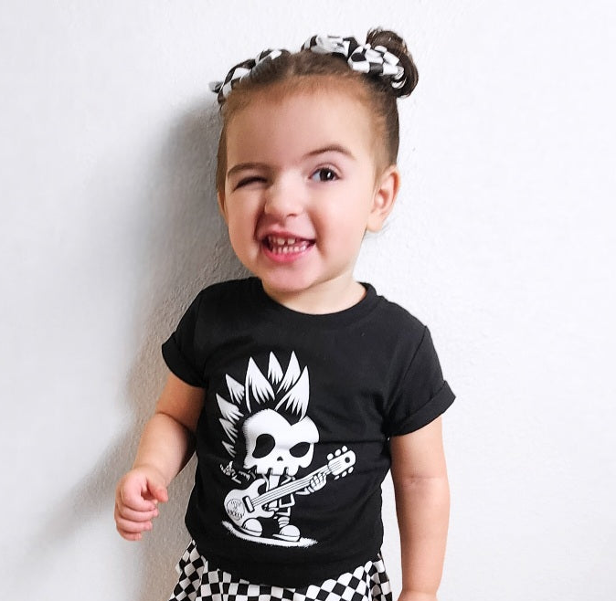 black kids graphic t-shirt with skeleton with a mohawk playing the guitar, little rocker clothing rock style outfit for toddlers and kids outdoors rear view