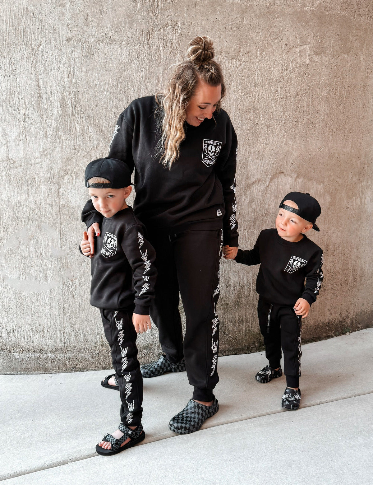 mom and sons wearing matching black aftershock crew neck sweatshirts and joggers set lightning bolt and rock hand print little rocker clothing adult and kids outfits