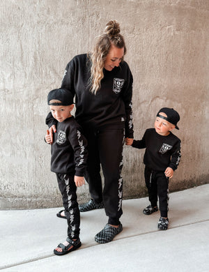 mom and sons wearing matching black aftershock crew neck sweatshirts and joggers set lightning bolt and rock hand print little rocker clothing adult and kids outfits