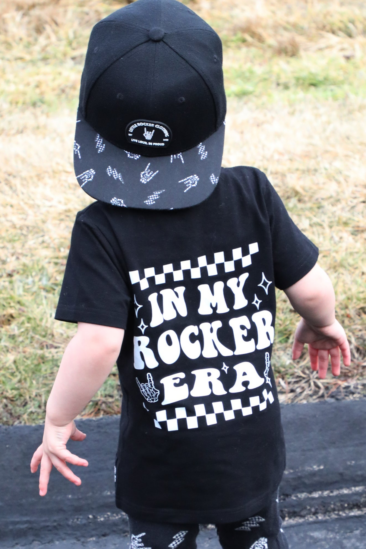 black kids graphic t-shirt with in my rocker era checkerboard detail, little rocker clothing rock style outfit for toddlers and kids outdoors rear view