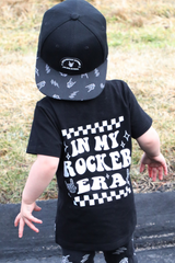 black kids graphic t-shirt with in my rocker era checkerboard detail, little rocker clothing rock style outfit for toddlers and kids outdoors rear view