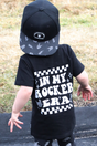 black kids graphic t-shirt with in my rocker era checkerboard detail, little rocker clothing rock style outfit for toddlers and kids outdoors rear view