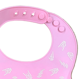 A close-up of a pink silicone baby bib with white printed cartoon characters, featuring a flexible neck strap with snap fasteners.