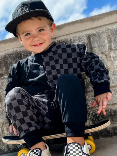 young boy wearing black kids sweat set with checkered pattern while sitting on a skateboard, little rocker clothing rock style outfit 