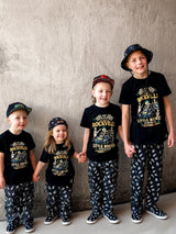 Group of kids wearing the welcome to rockville kids graphic tee collaboration, rock festival band style t shirt for kids, black rocker tee with bold music design, little rocker clothing festival apparel