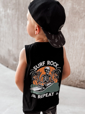 Toddler wearing black Little Rocker Clothing tank top with skeleton surfing graphic and “Surf Rock Repeat” design, paired with black snapback hat