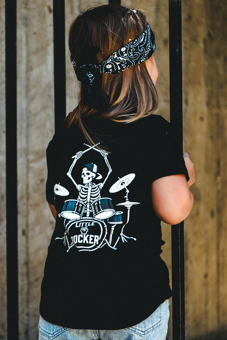 black kids graphic t-shirt with skeleton playing drums, little rocker clothing rock style outfit for toddlers and kids outdoors rear view