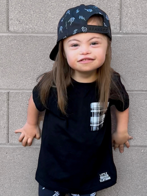 toddler boy with long hair wearing a black little rocker clothing tshirt with a plaid pocket