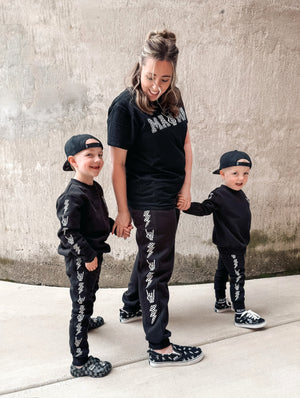 mom and sons wearing matching joggers featuring lightning bolt and rock hand print little rocker clothing adult and kids outfits