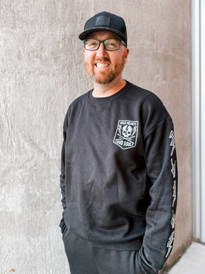 adult man wearing matching black aftershock crew neck sweatshirts and joggers set lightning bolt and rock hand print little rocker clothing adult and kids outfits