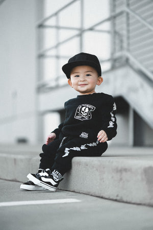 1 year old wearing matching black aftershock crew neck sweatshirts and joggers set lightning bolt and rock hand print little rocker clothing adult and kids outfits