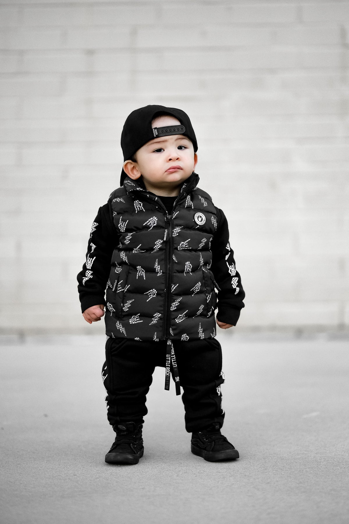lifestyle image of the Kids black puffer vest with Bolted Bones design featuring skeleton hand rock on graphic and lightning bolts, rocker style outerwear for kids
