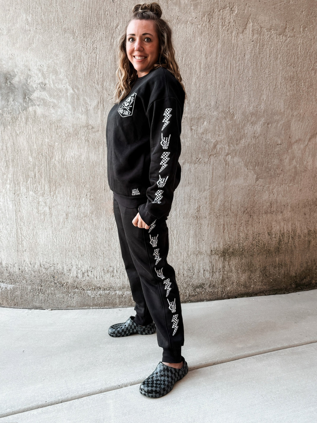 adult woman wearing matching black aftershock crew neck sweatshirts and joggers set lightning bolt and rock hand print little rocker clothing adult and kids outfits