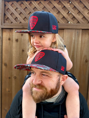 Kid and adult wearing Little Rocker Clothing black and red Scene Sampler snapback hat featuring bold music inspired design, adjustable snapback cap for kids and adults, edgy rock style apparel accessory