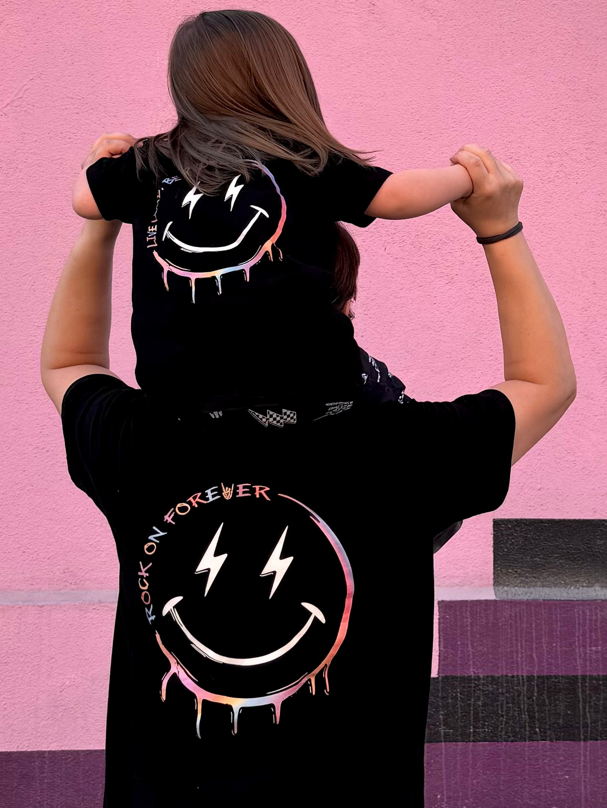adult and child wearing black graphic t-shirt with pastel text in a smiley face, little rocker clothing punk rock toddler and adult outfit 