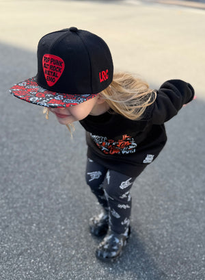 Kid wearing black and red Scene Sampler snapback hat featuring bold music inspired design, adjustable snapback cap for kids and adults, edgy rock style apparel accessory