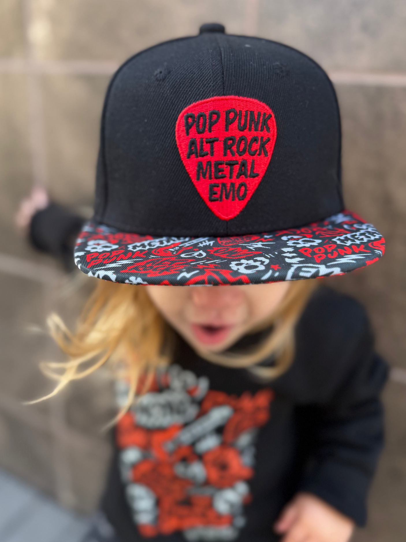 Kid wearing black and red Scene Sampler snapback hat featuring bold music inspired design, adjustable snapback cap for kids and adults, edgy rock style apparel accessory