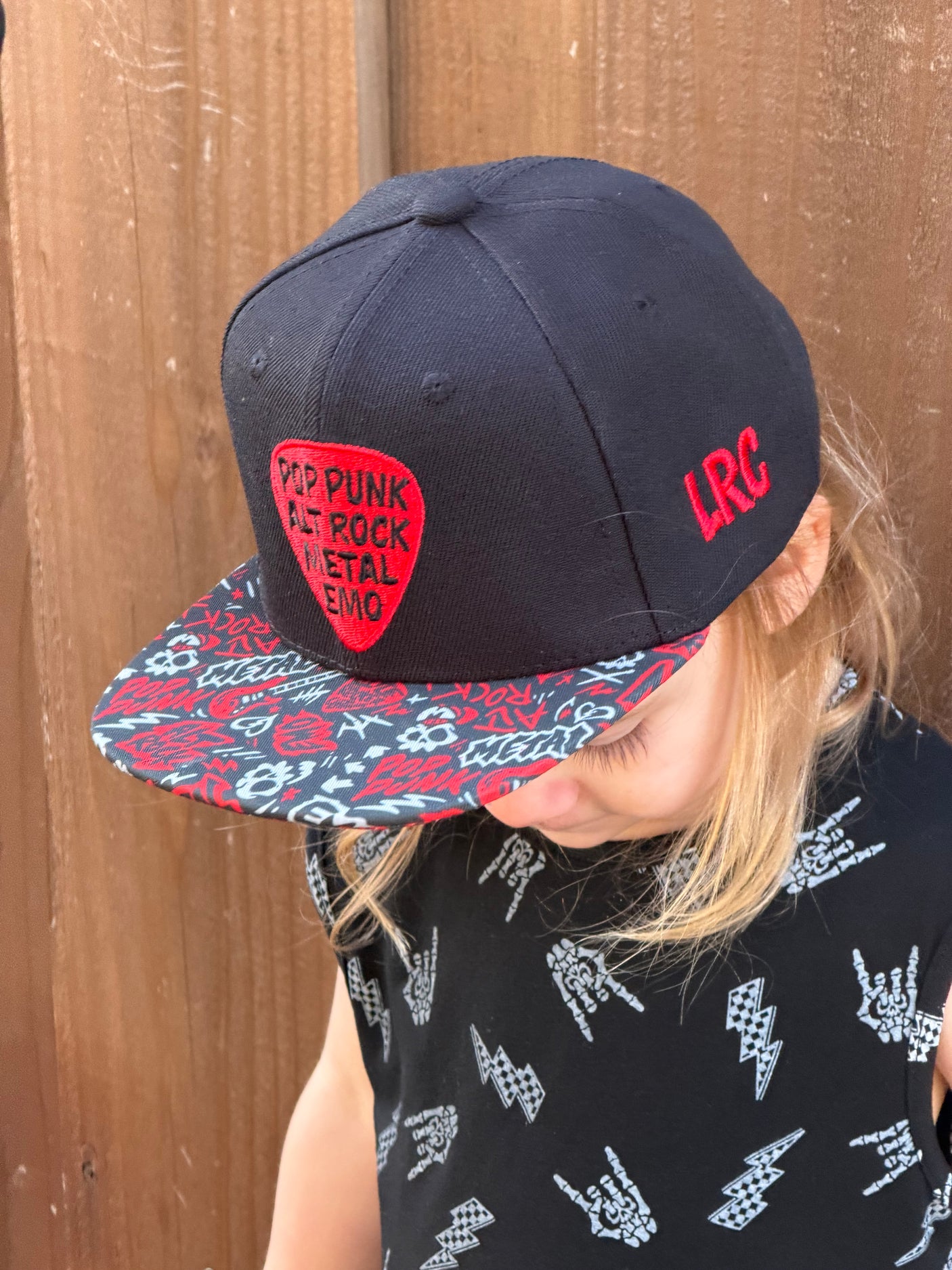 Kid wearing black and red Scene Sampler snapback hat featuring bold music inspired design, adjustable snapback cap for kids and adults, edgy rock style apparel accessory