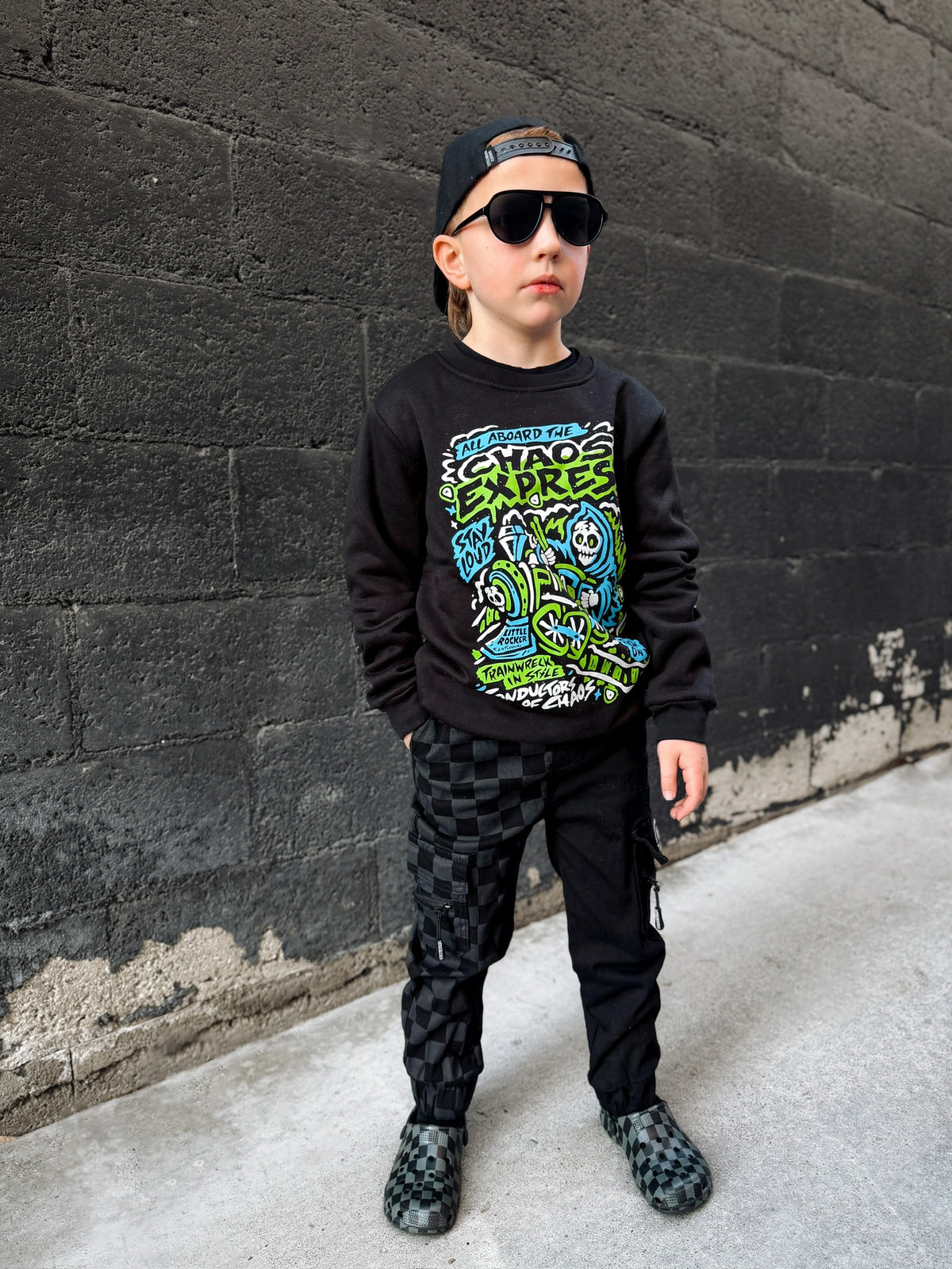 Young boy wearing Kids black Scene Sampler crew neck sweatshirt featuring pop punk, emo, and alt rock graphic with train illustration, rocker style kids apparel