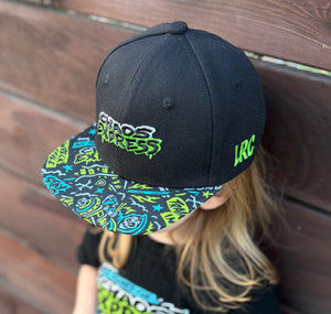Kid wearing Little Rocker Clothing chaos express blue and green snapback hat, adjustable snapback cap for kids and adults, edgy rock music inspired apparel accessory