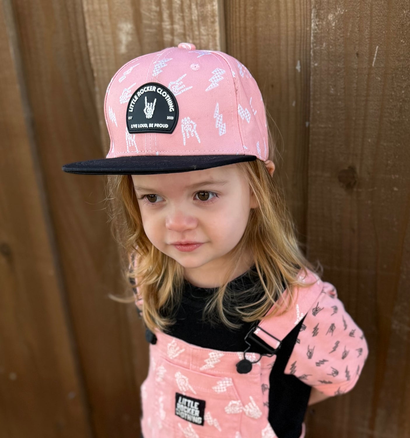 Kid wearing Little Rocker Clothing pink and black rock on and lightening bolt snapback hat, adjustable snapback cap for kids and adults, edgy music inspired apparel accessory