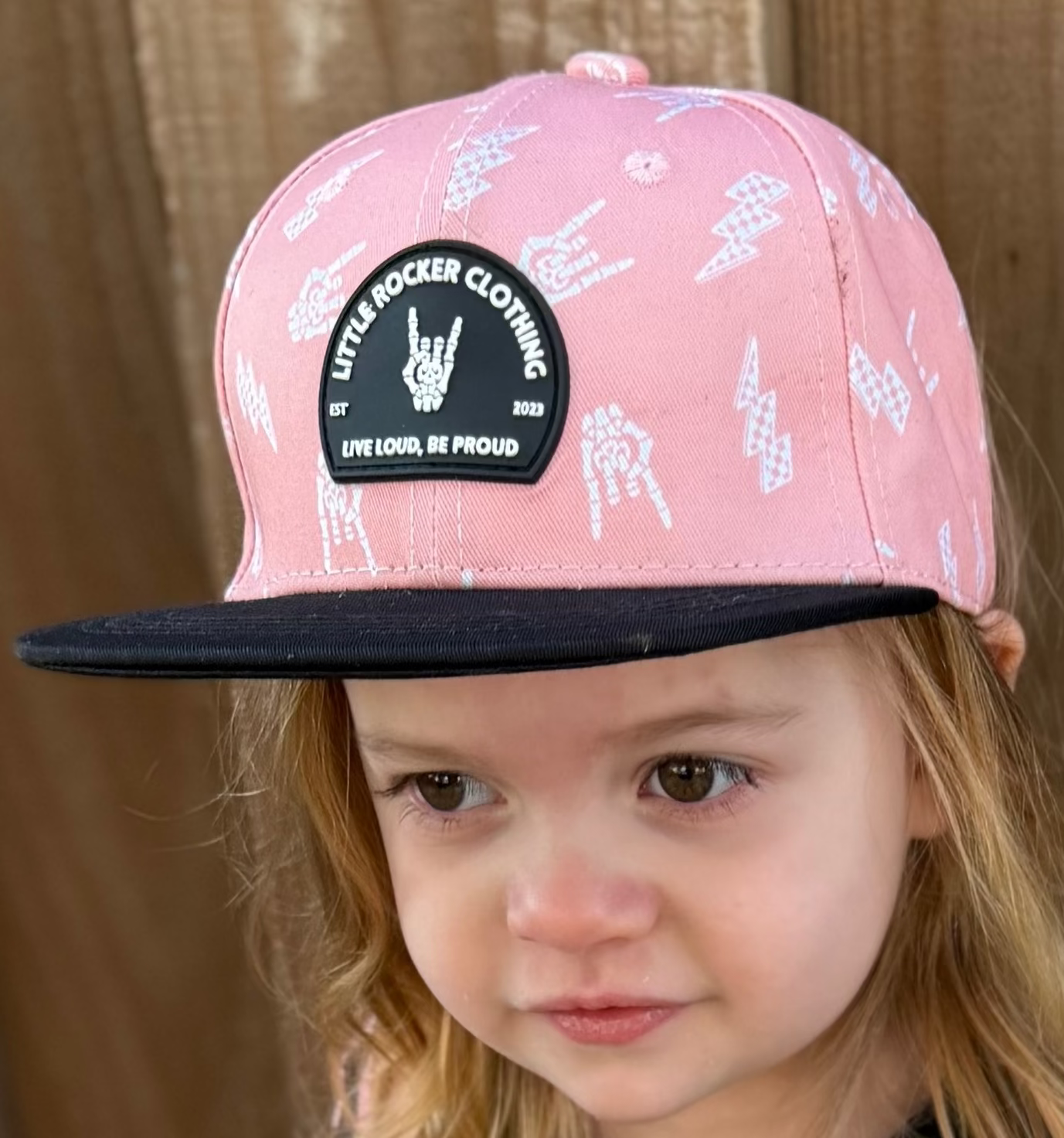 Kid wearing pink and black rock on and lightening bolt snapback hat, adjustable snapback cap for kids and adults, edgy music inspired apparel accessory