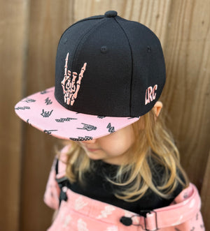 Kid wearing Little Rocker Clothing pink and black rock on snapback hat, adjustable snapback cap for kids and adults, edgy music inspired apparel accessory