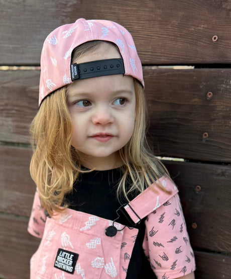 Kid wearing pink and black rock on and lightening bolt snapback hat, adjustable snapback cap for kids and adults, edgy music inspired apparel accessory