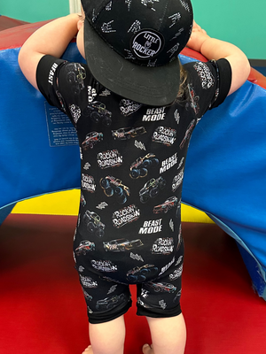 infant girl wearing black bamboo pajamas with a monster truck pattern and a backwards black snapback, little rocker clothing rock style outfit 