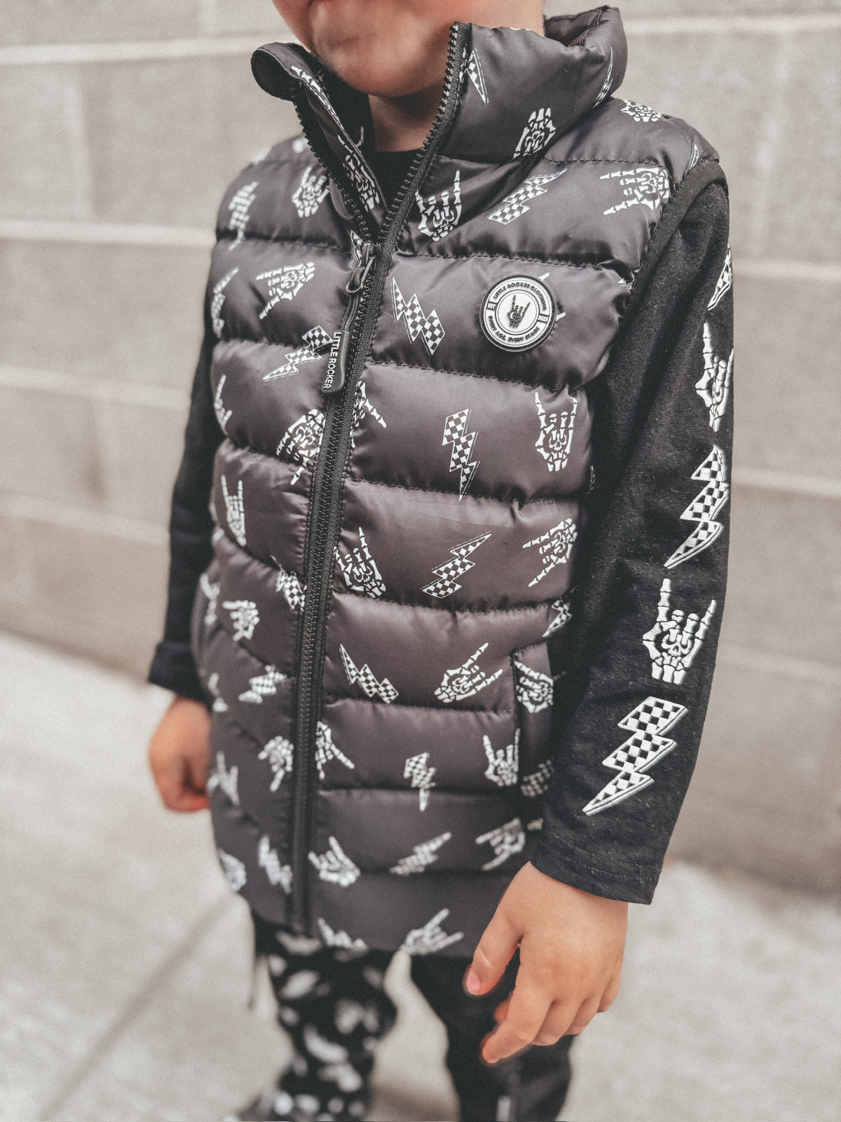 close up of  Kids black puffer vest with Bolted Bones design featuring skeleton hand rock on graphic and lightning bolts, rocker style outerwear for kids